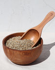 Photo showing rye grain in small wooden bowl, with wooden scoop . White, textured background