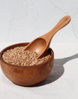 Photo showing spelt grain in small wooden bowl, with wooden scoop . White, textured background