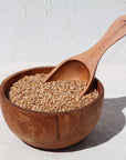 Photo showing wheat grain in small wooden bowl, with wooden scoop . White, textured background